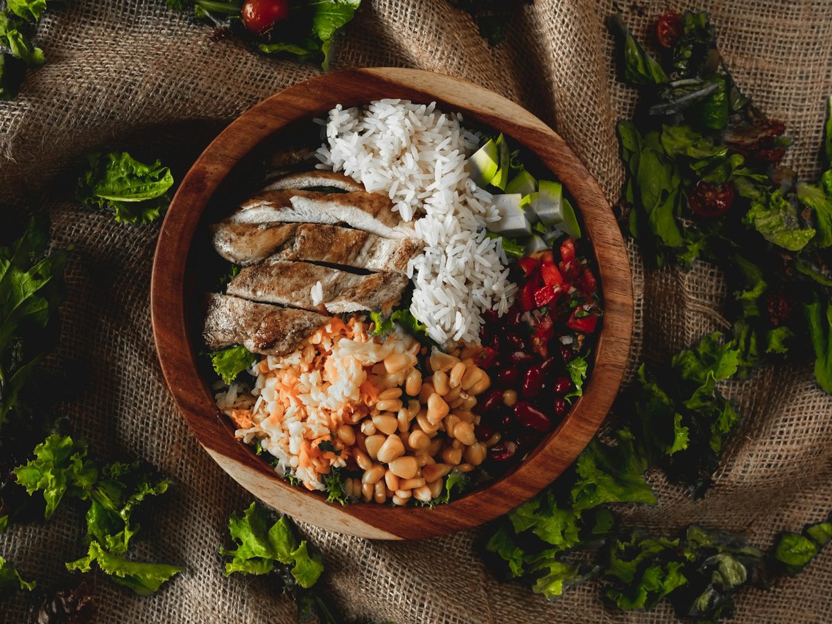 Bol en bois garni de riz, poulet grillé, haricots, carottes râpées et salade